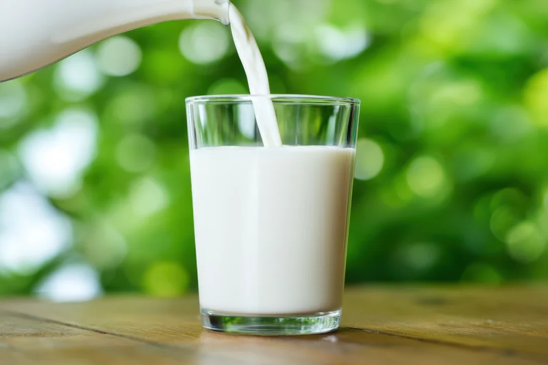 Glass of milk being poured featuring a clear cylindrical glass