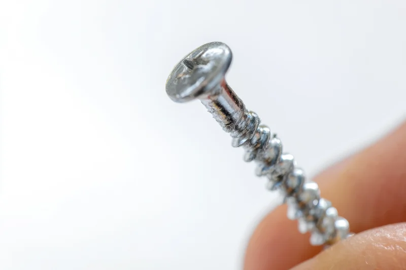 Hand holding a shiny metallic screw against white background