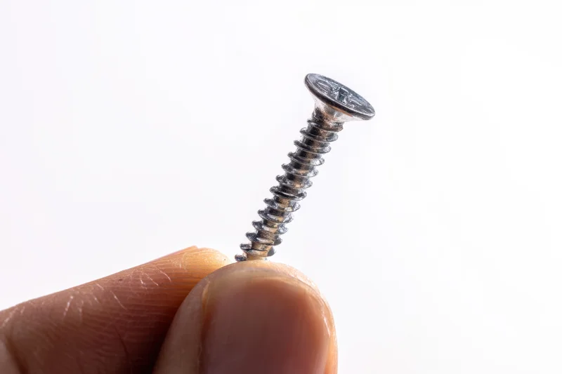 Hand holding a metallic screw with shiny surface against white background
