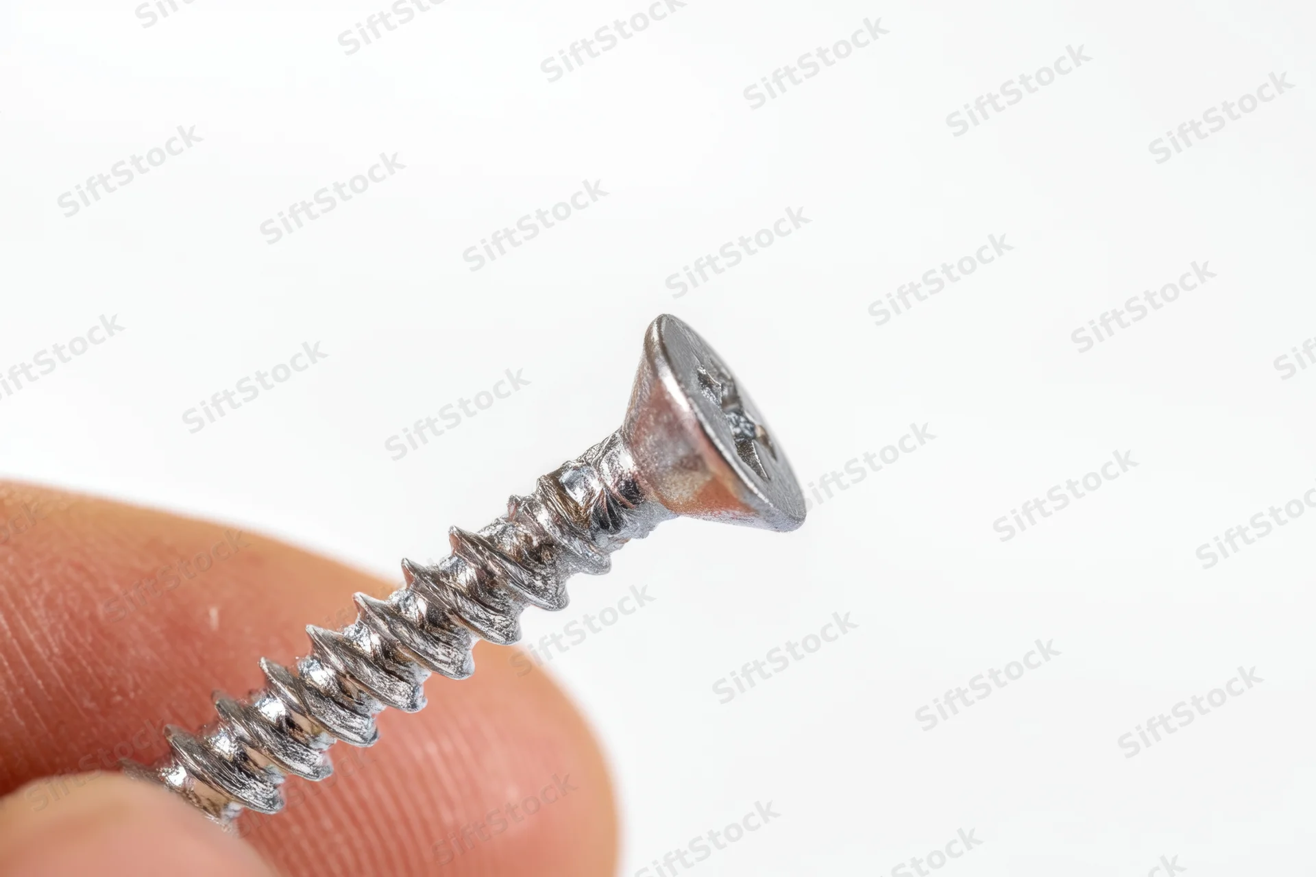 Hand holding a shiny metallic screw with Phillips head against white background