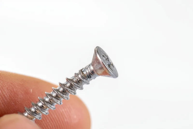 Hand holding a shiny metallic screw with Phillips head against white background