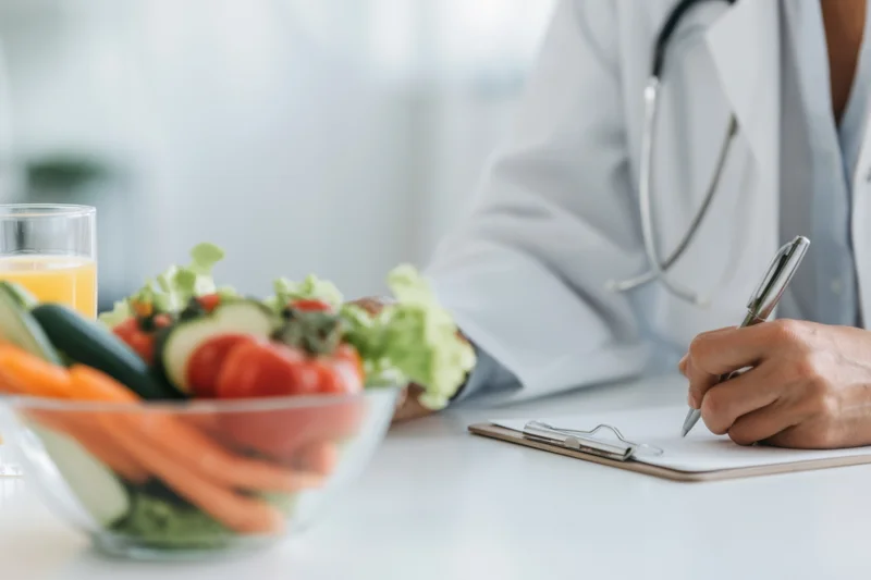 Doctor writing notes during nutrition consultation with vegetables on desk
