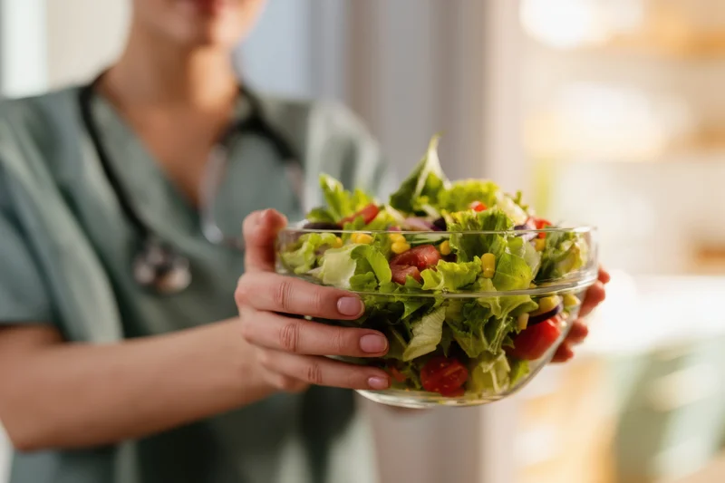 Healthcare professional holding a glass bowl of fresh salad in a kitchen setting