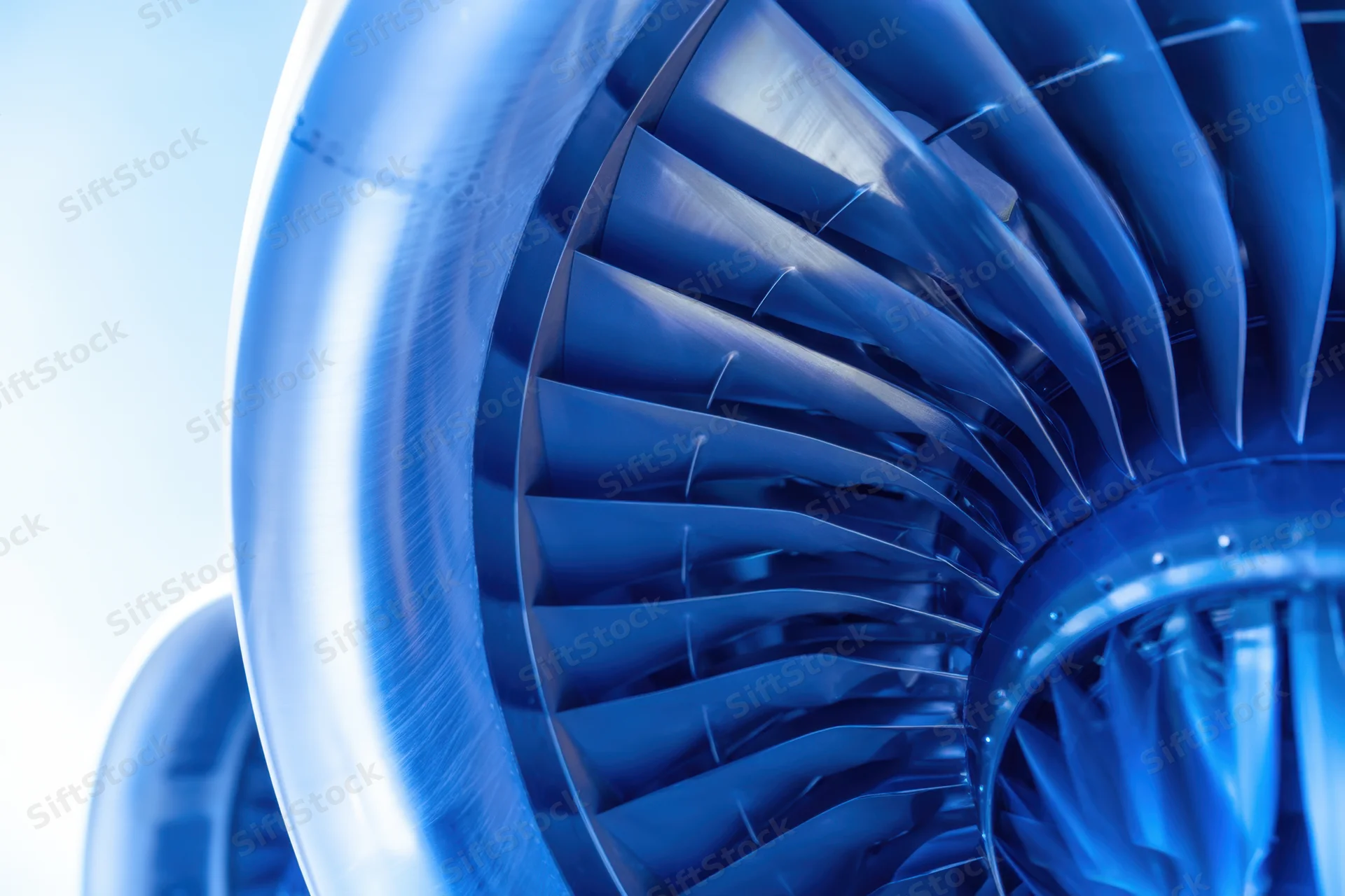 Closeup of jet engine turbine blades showing curved metallic structure in blue tone