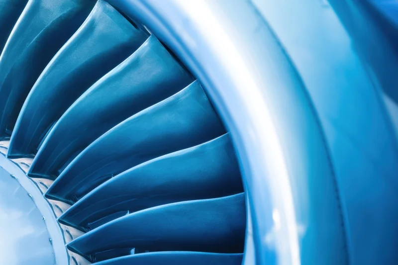 Closeup of jet engine turbine blades arranged in circular pattern showing metallic blue blades and smooth casing