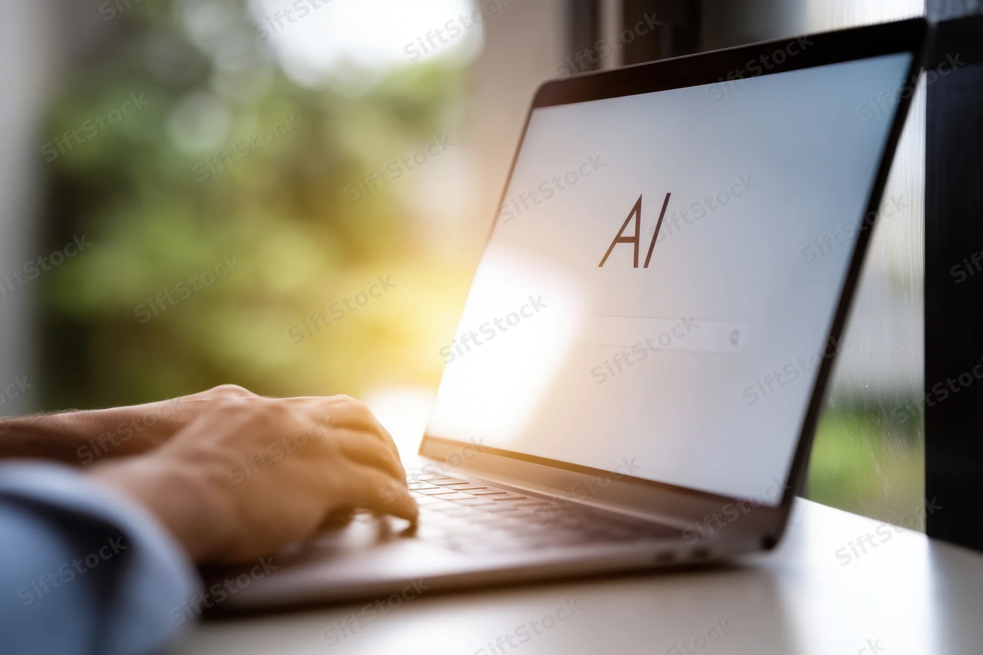 Hand typing on laptop keyboard with ai displayed on screen near window