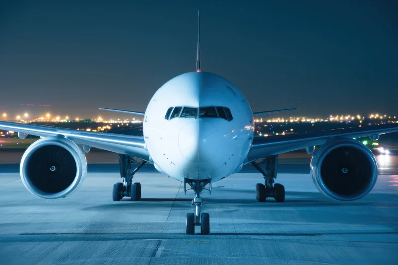 Large commercial airplane viewed head-on on airport tarmac at night with runway lights in background