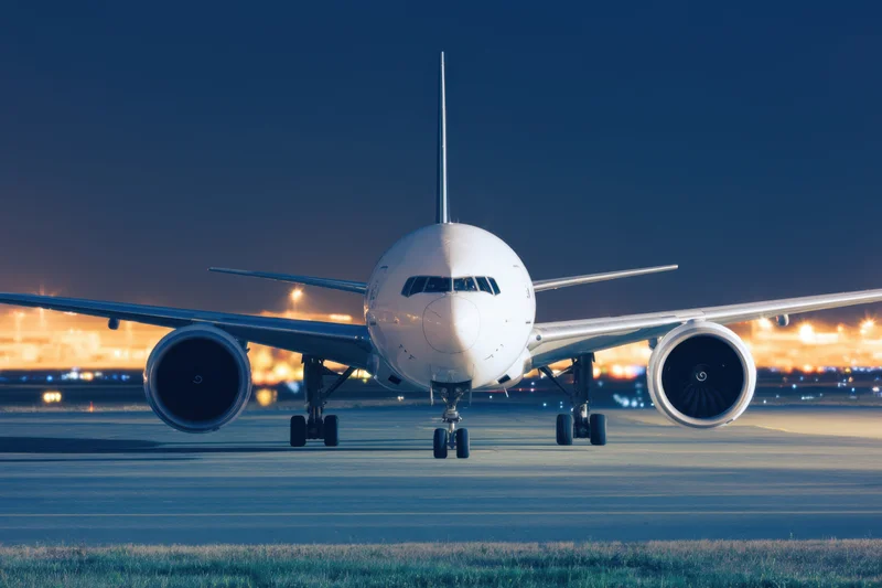 Large commercial airplane viewed head-on on airport tarmac at dusk with city lights in background