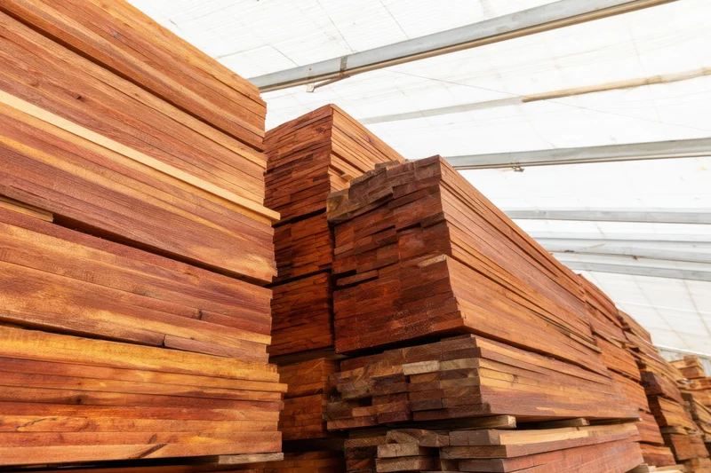 Stacks of lumber planks arranged in a storage yard under a translucent roof