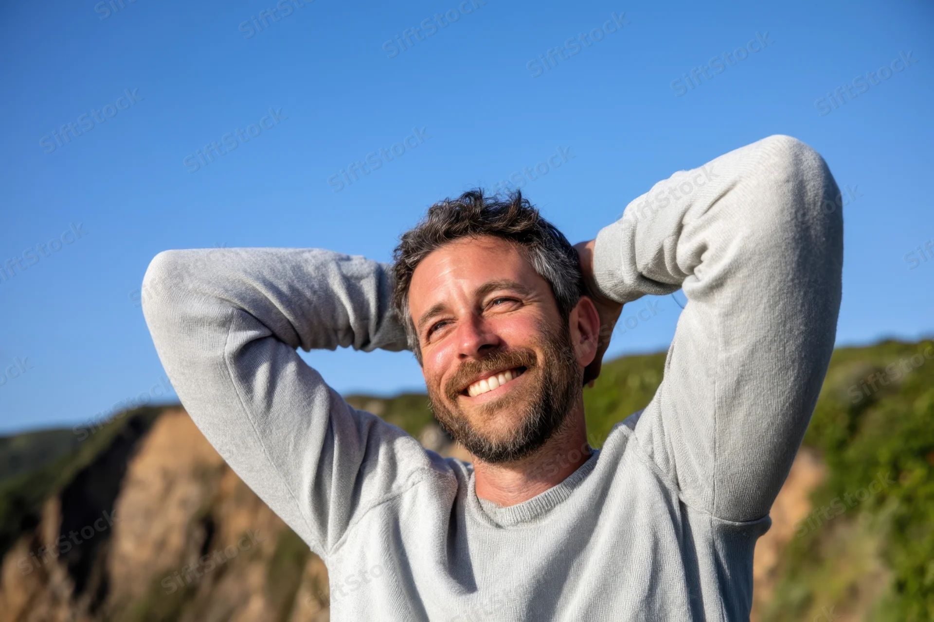 Man smiling with arms behind his head outdoors in nature