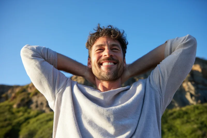 Man smiling with arms behind his head outdoors in natural landscape