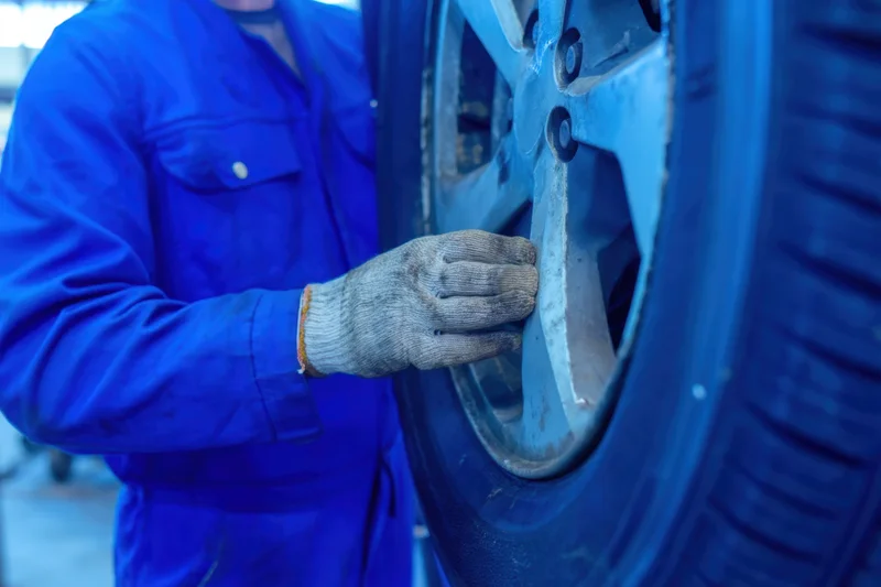 Mechanic inspecting car wheel in workshop wearing blue coveralls and gloves