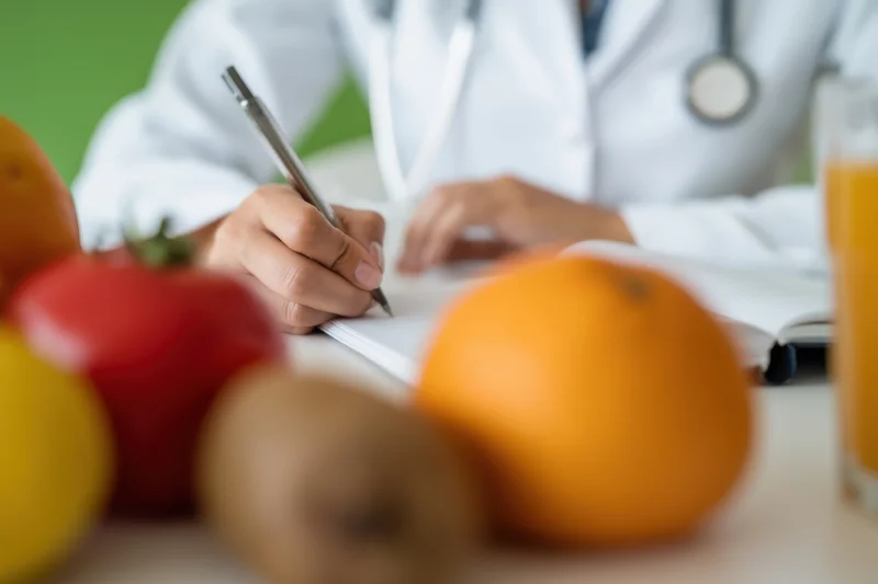 Doctor writing in notebook at desk with fresh fruit and juice in foreground