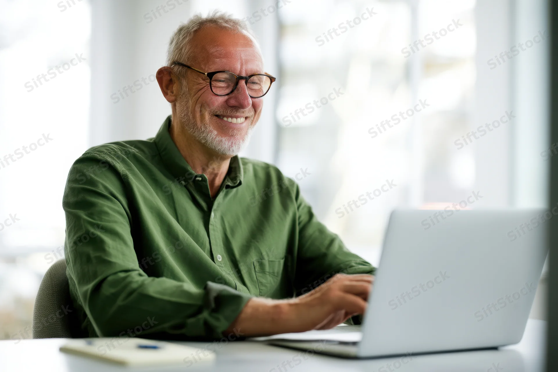 Senior man smiling while working on laptop at office desk