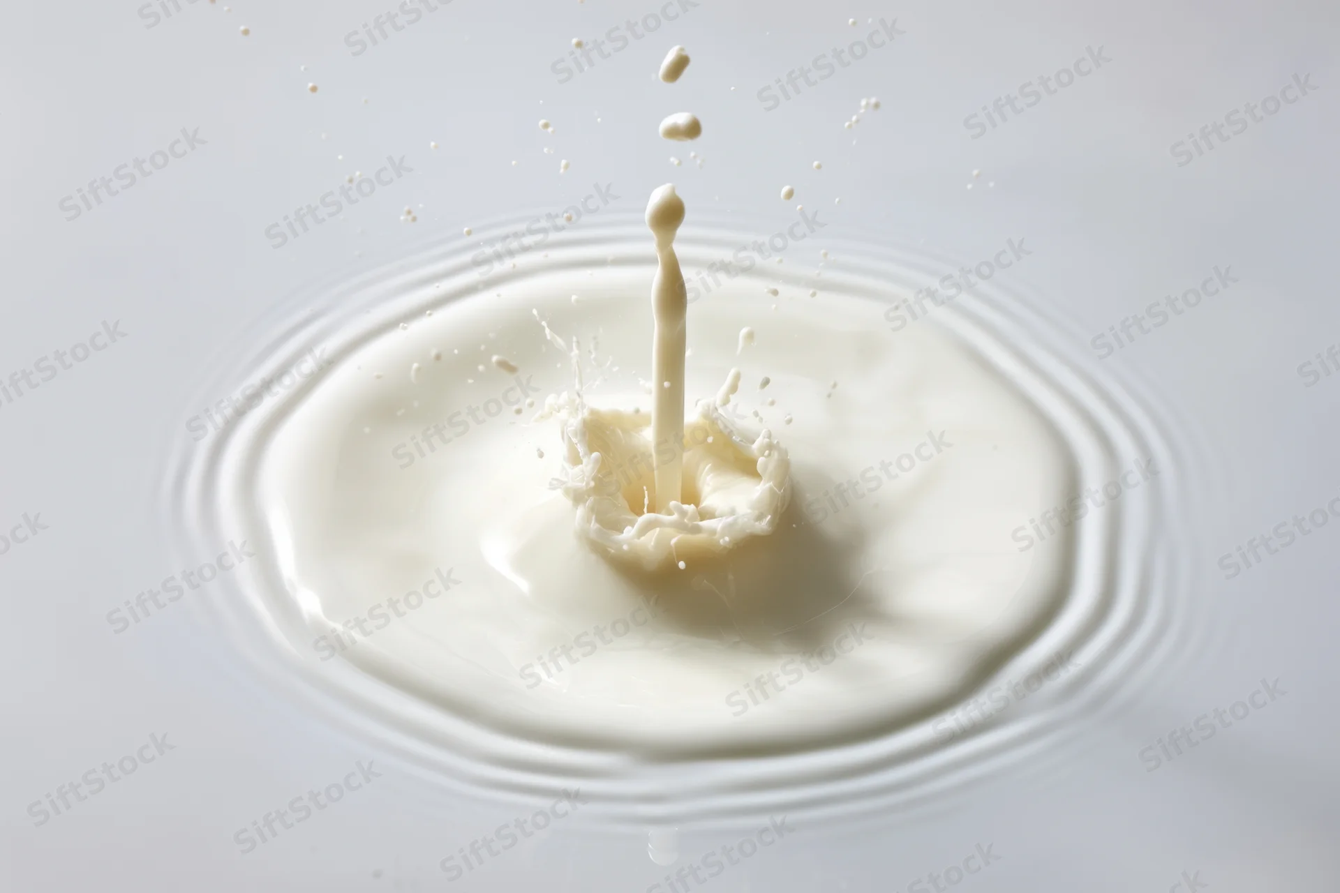 Milk splash captured mid-air with droplets flying outward on a white surface