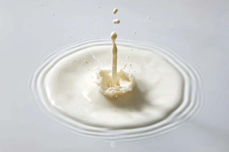 Milk splash captured mid-air with droplets flying outward on a white surface