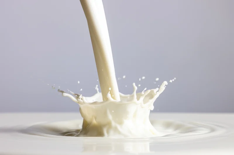 Smooth stream of milk cascading into a pool creating a splash and ripples on a plain surface