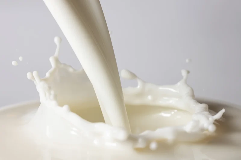 Smooth stream of milk cascading into a pool creating a splash with crown-like droplets against a plain background