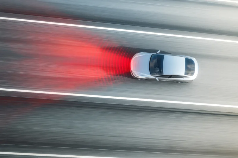 Silver modern car with advanced technology driving on highway at high speed, emitting red sensor waves from rear