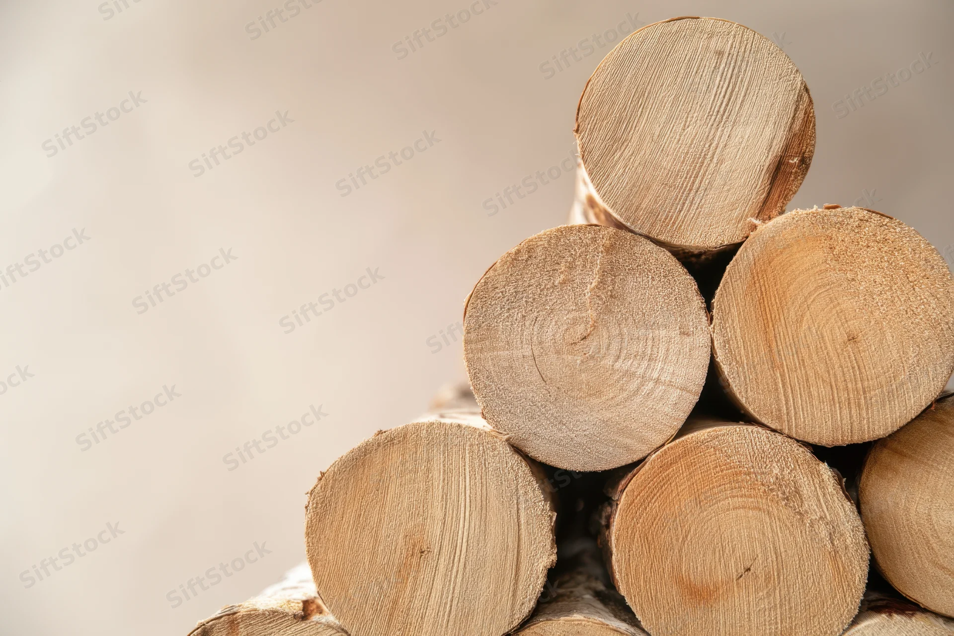 Neatly stacked wooden logs arranged in a pyramid shape with visible grain and bark edges against a plain light background