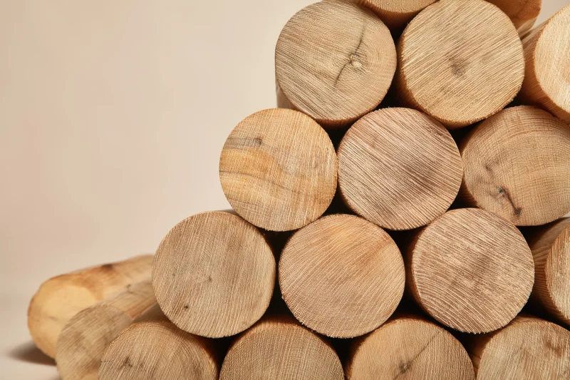 Neatly stacked wooden logs arranged in a pile with smooth cut ends showing natural grain and texture against a neutral background