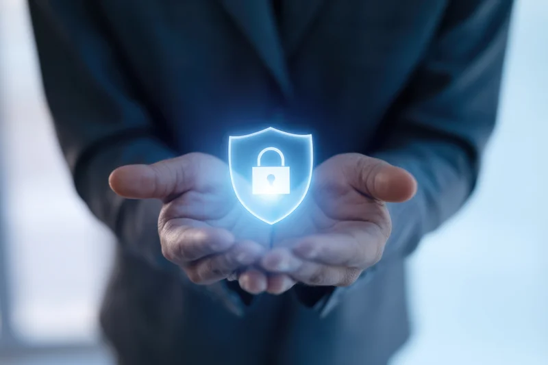 Hands cradling a glowing holographic shield with a lock symbol in an office setting