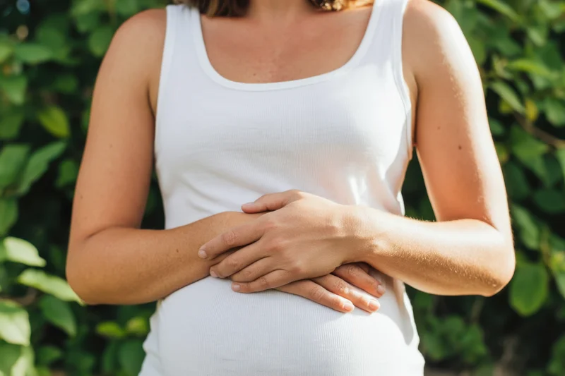 Pregnant woman holding her stomach outdoors with green foliage in the background