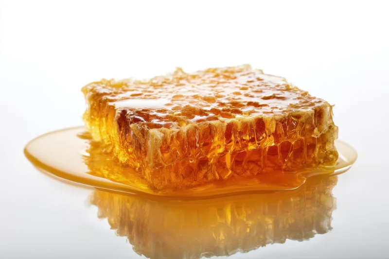 Piece of honeycomb with honey dripping onto a glossy reflective surface