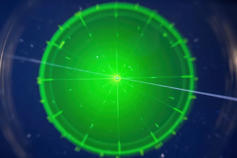 Green circular radar display with glowing center and radial lines on dark background