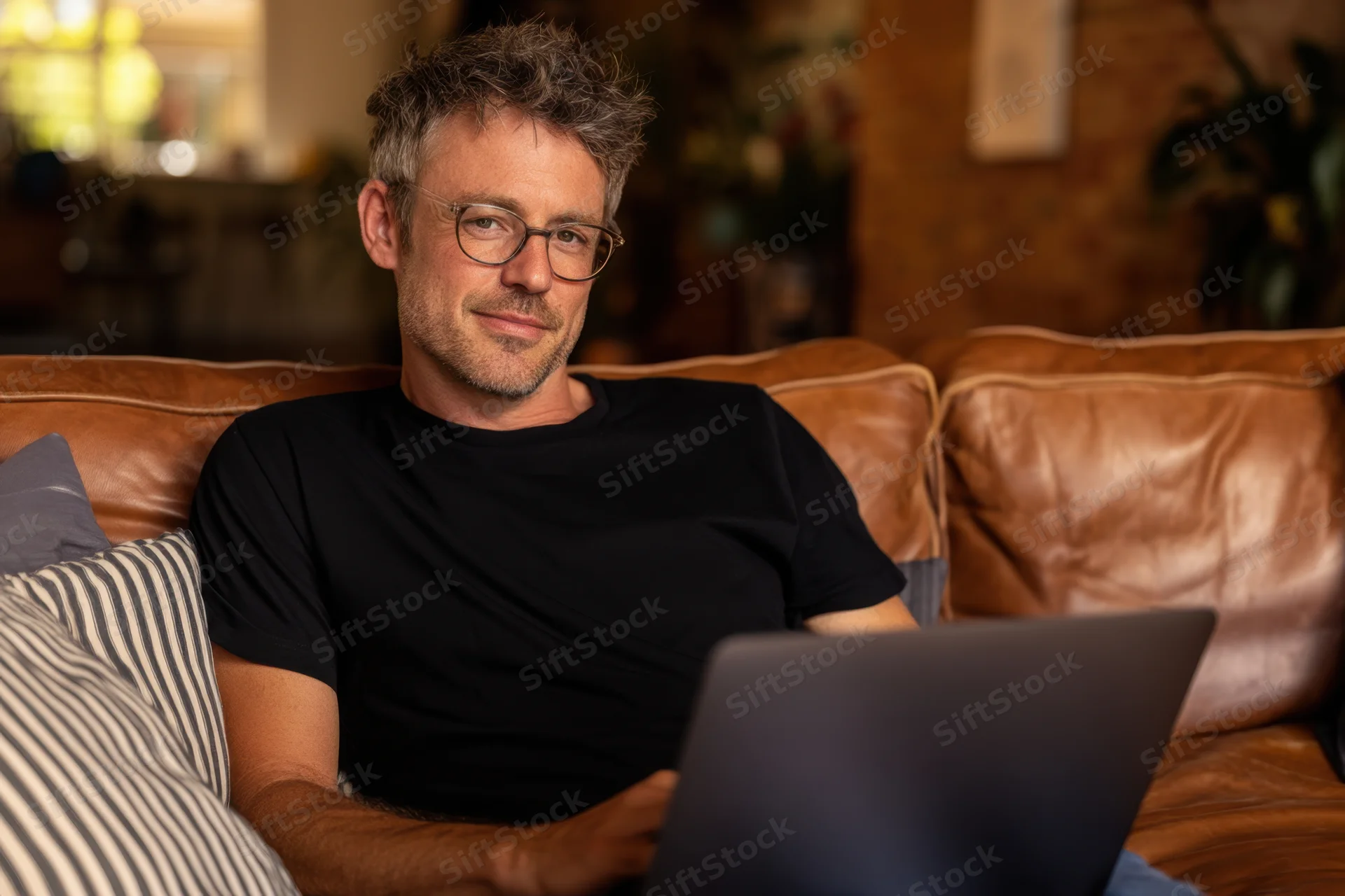 Man sitting relaxed on brown leather couch using laptop at home