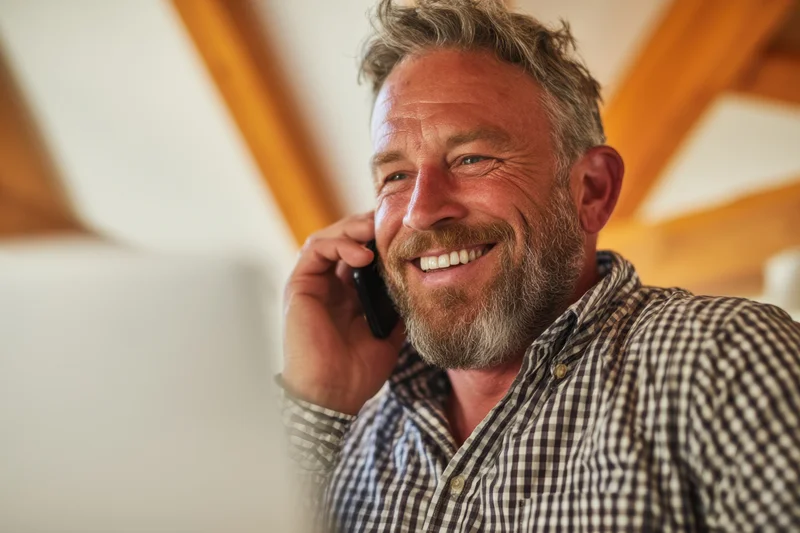 Smiling man in checkered shirt talking on phone indoors