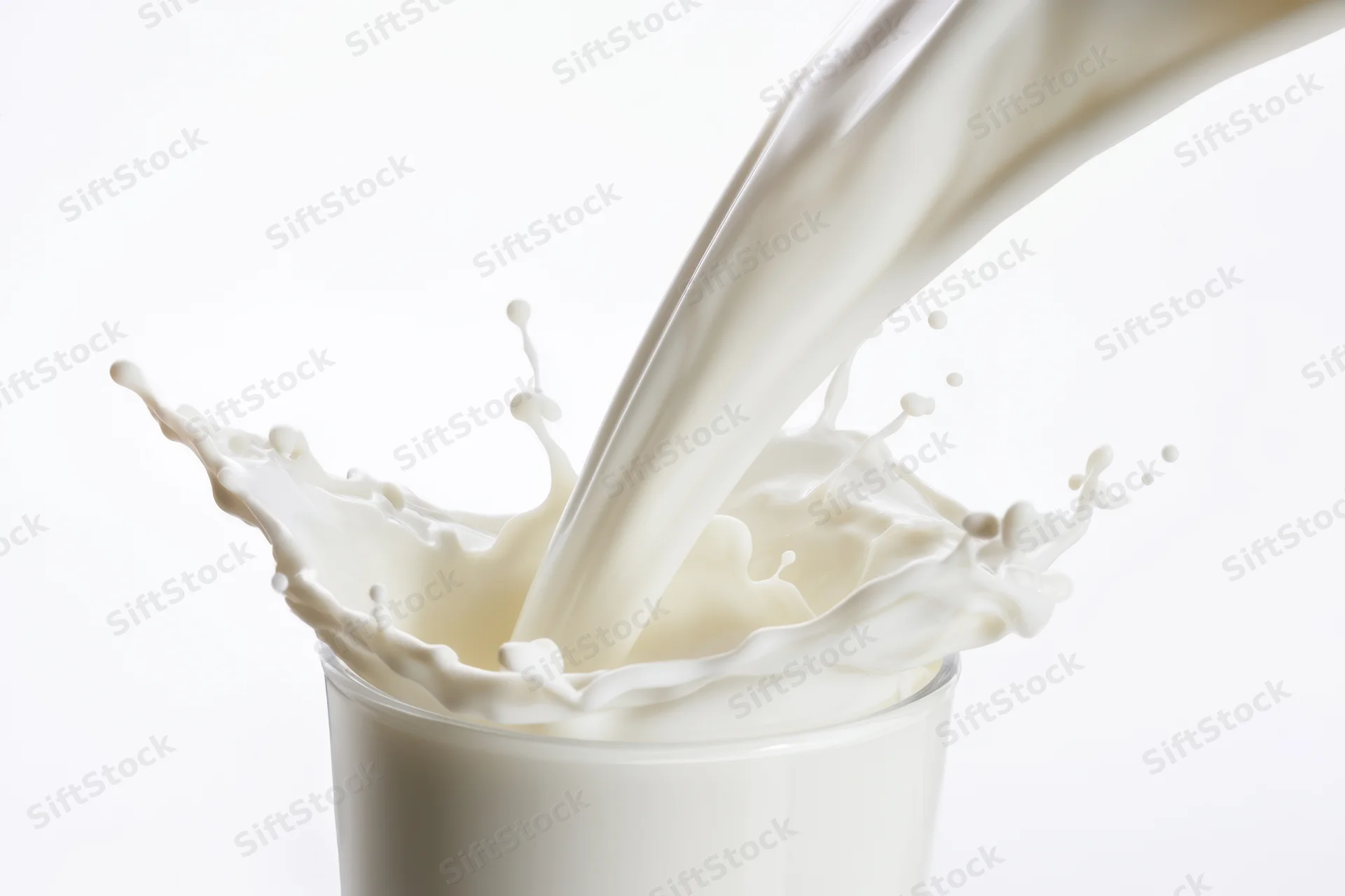 Milk pouring into a glass creating a splash with flowing waves and droplets
