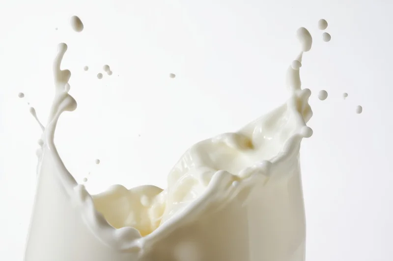Milk splash forming a crown with flowing waves and airborne droplets against a white background