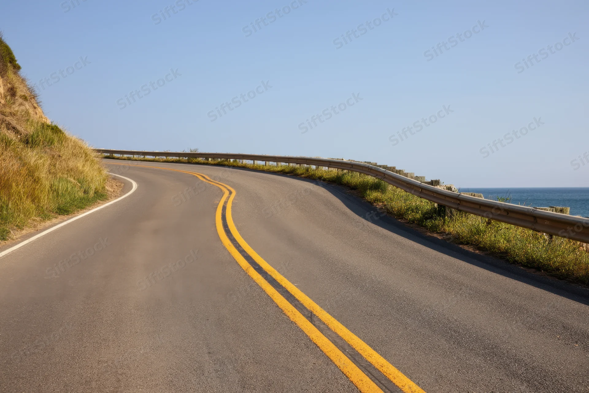 Winding asphalt road curving along a coastal cliff with ocean view and guardrail