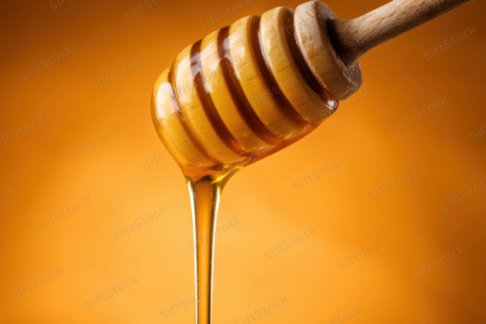 Wooden honey dipper dripping golden honey against orange background