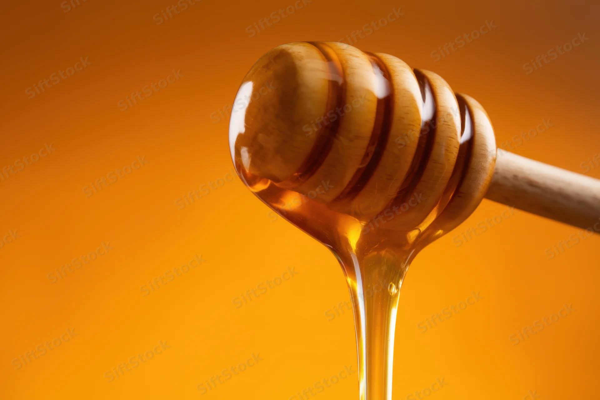 Wooden honey dipper dripping golden honey against orange background
