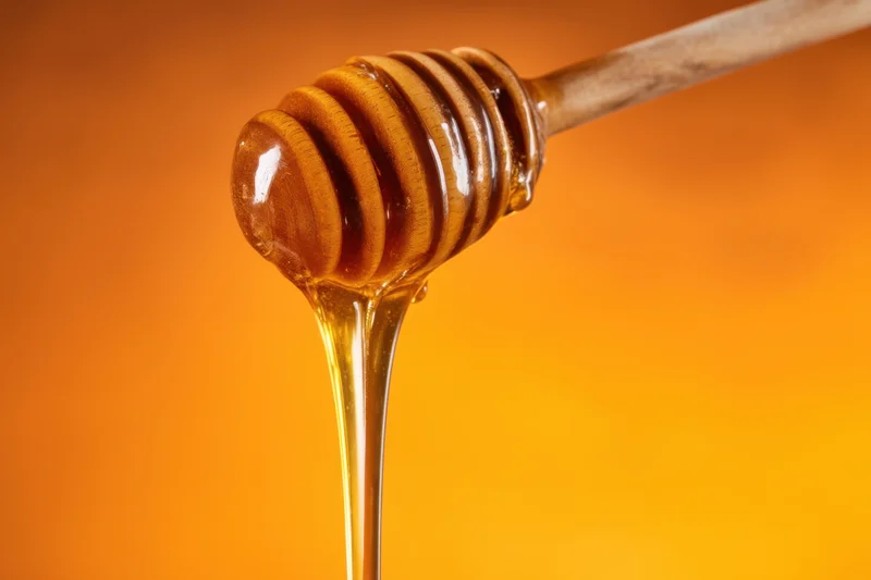 Wooden honey dipper dripping golden honey against warm orange background
