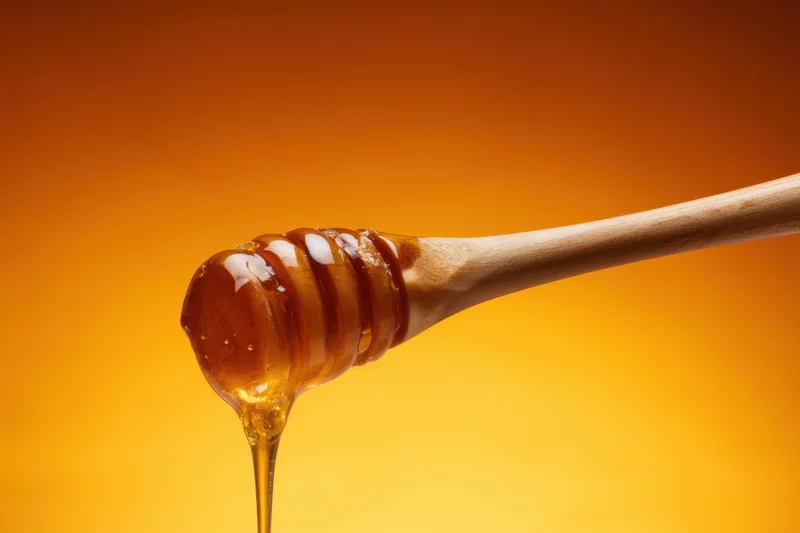 Wooden honey dipper dripping golden honey against warm orange background