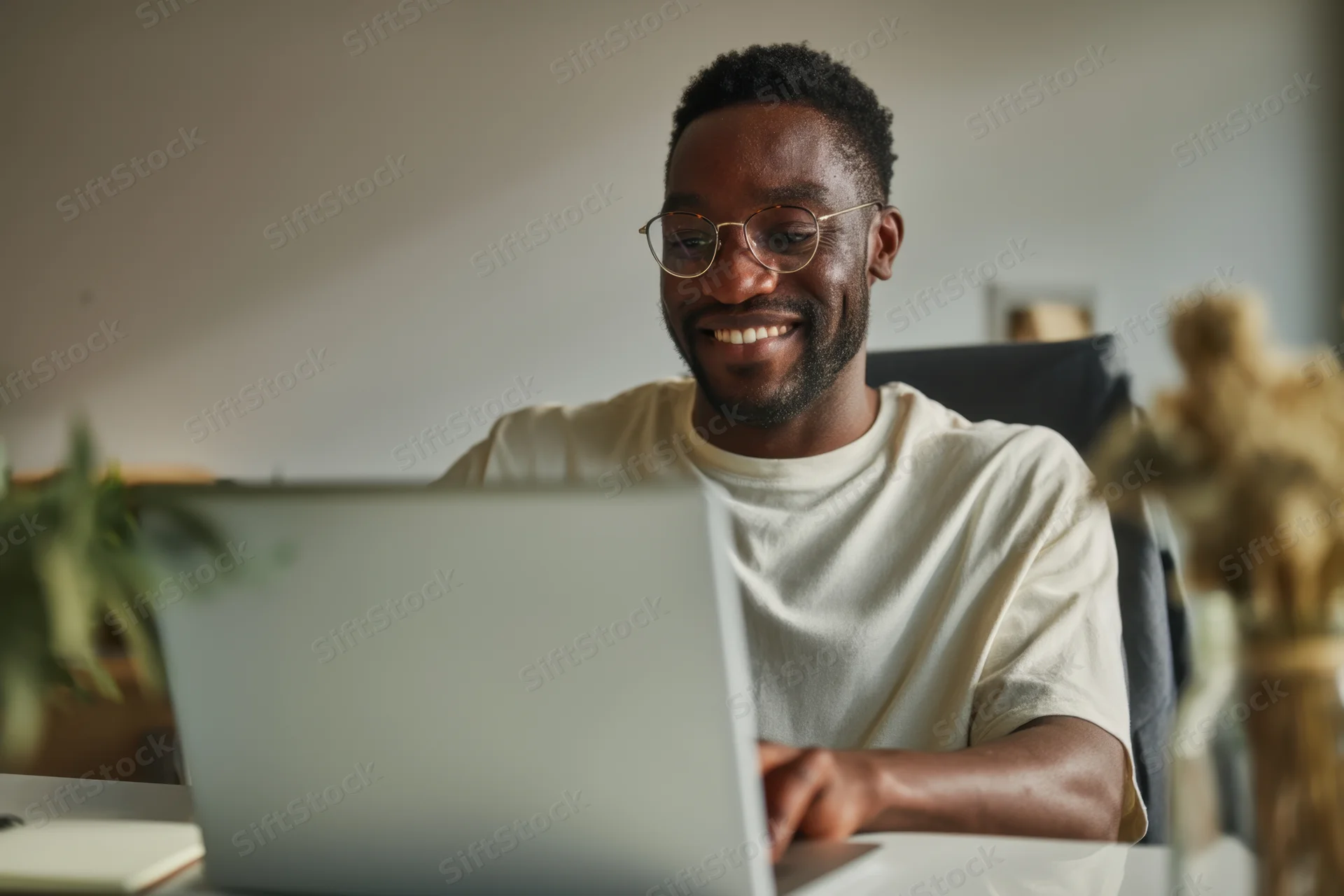 Young black man smiling while working on laptop at home office desk