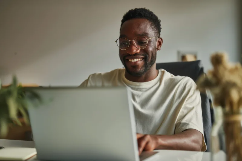 Young black man smiling while working on laptop at home office desk