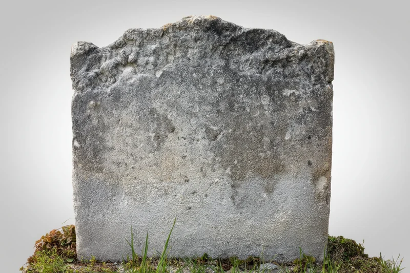 Weathered gravestone standing in grass with moss at base against plain background