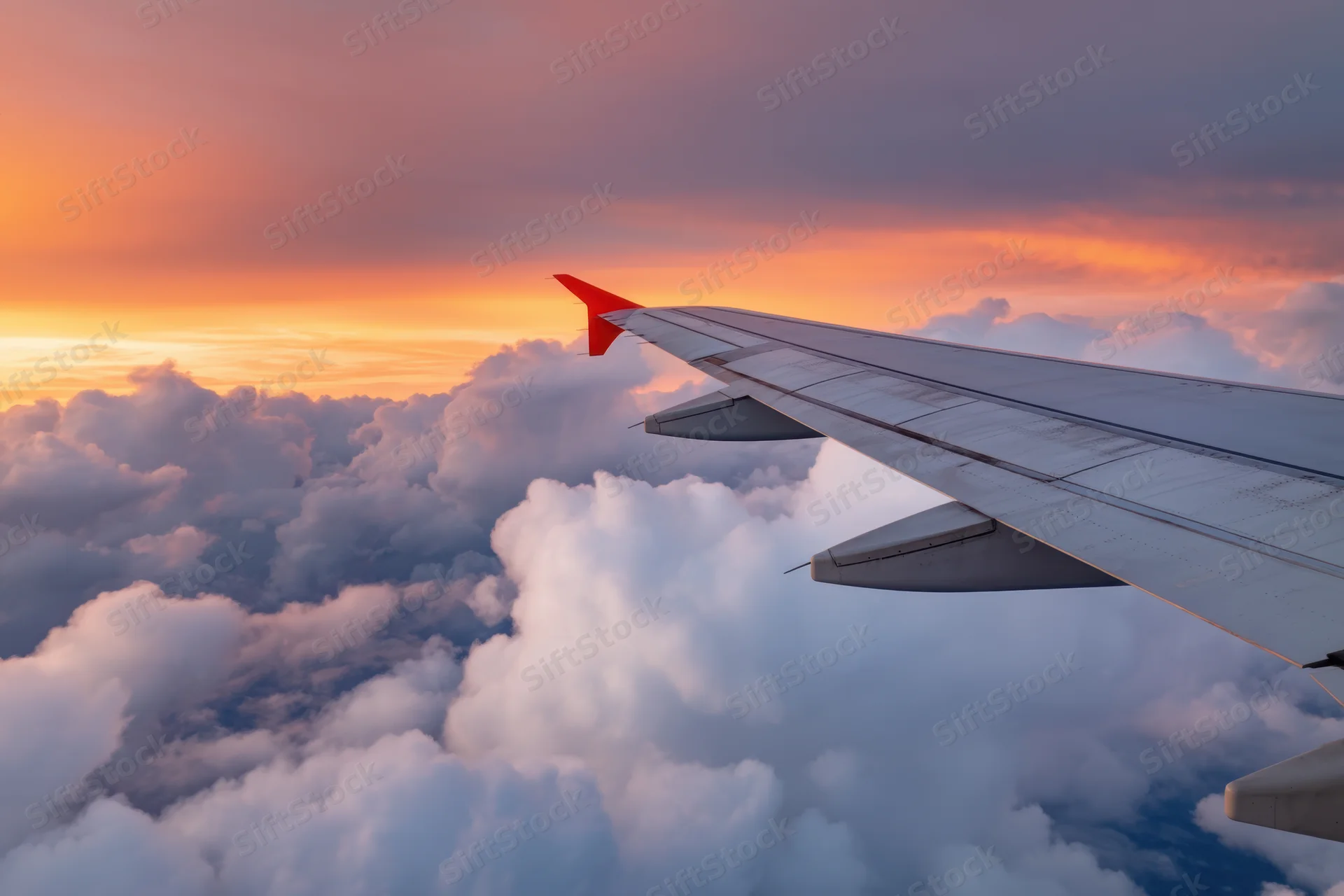 Airplane wing extending over fluffy clouds during sunset skyview