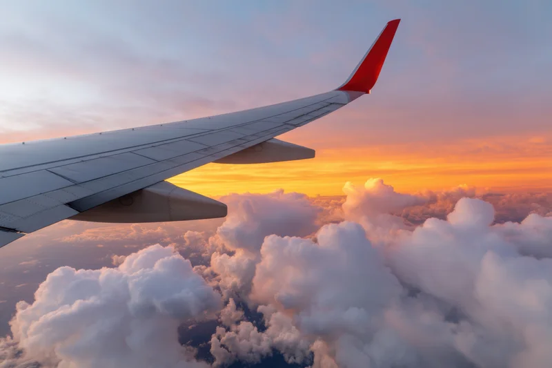 Airplane wing extending over fluffy clouds during sunset skyview