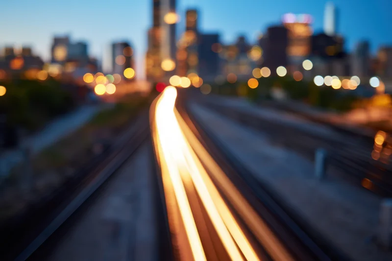 Train moving along tracks at dusk with blurred city lights in background