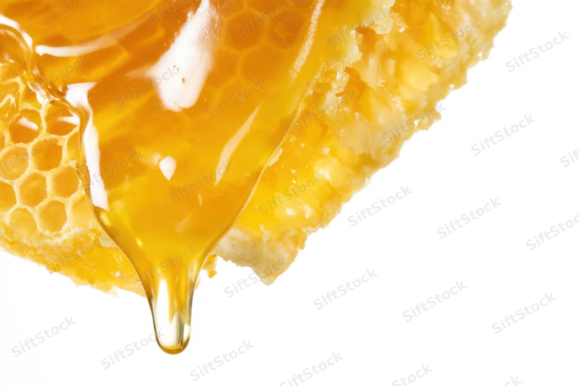 Golden honey dripping from a honeycomb against white background