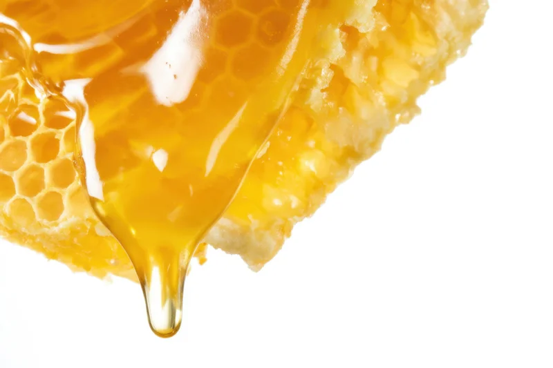 Golden honey dripping from a honeycomb against white background