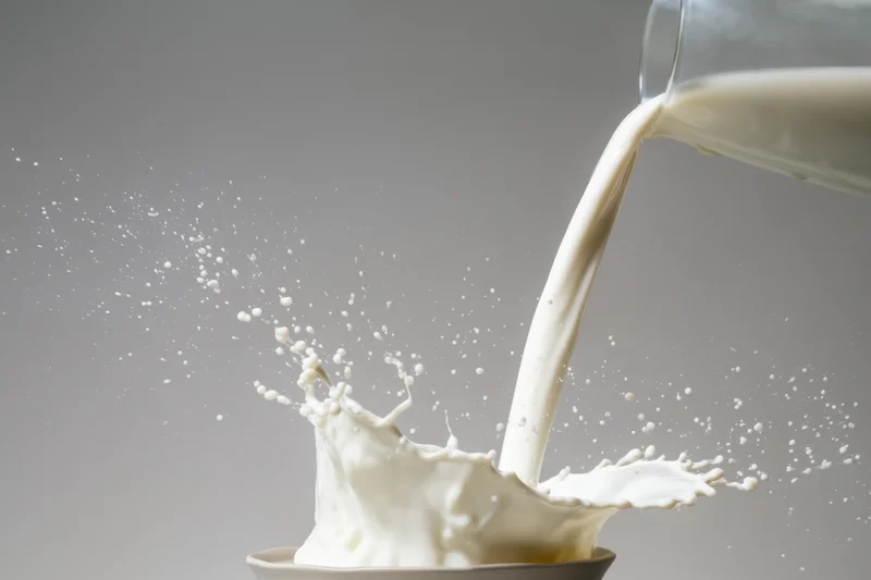 Milk being poured from a glass container into a bowl creating a splash