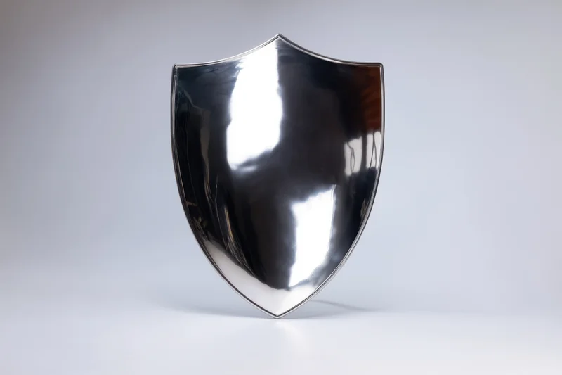 Polished metallic shield standing upright on a white surface with reflective surface and soft lighting