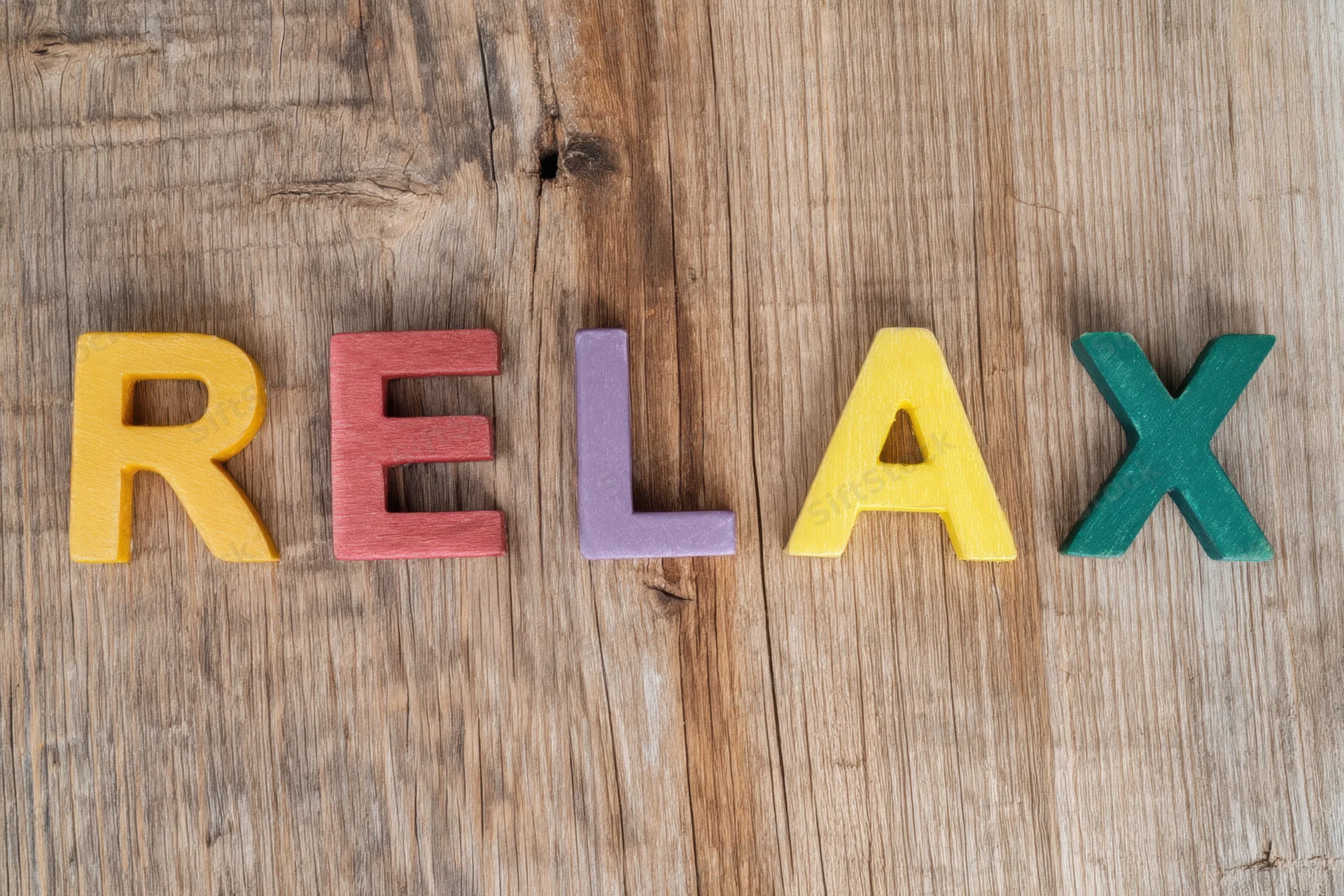 Colorful wooden letters spelling relax arranged on a rustic wood surface