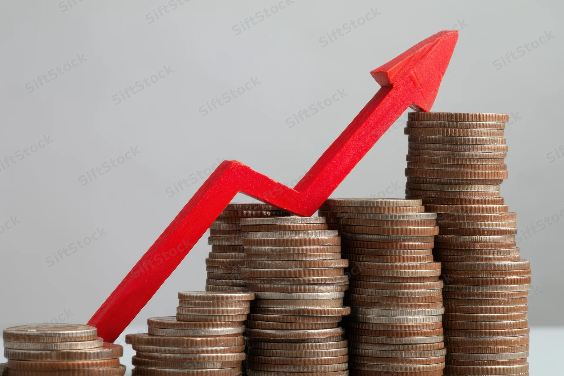 Stacked coins arranged in ascending order with a red arrow pointing upward across them